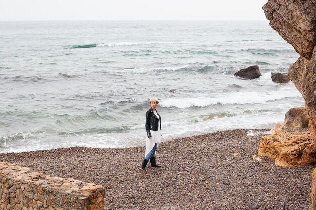 Hipster woman wearing dress and jacket walking near sea in autumn