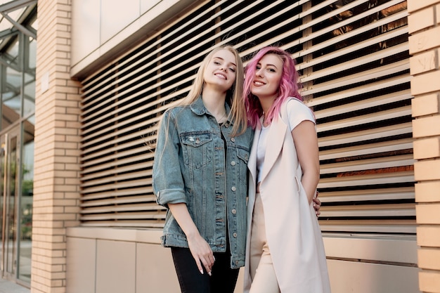 Hipster young adult friends embracing while hanging out in the city. Two young women laughing and walking enjoying carefree vacation lifestyle