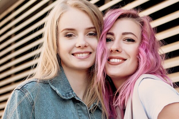 Hipster young adult friends embracing while hanging out in the city. Two young women laughing and walking enjoying carefree vacation lifestyle