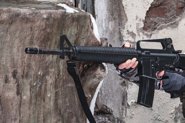 A hired soldier is aiming from a modern rifle near a wall.