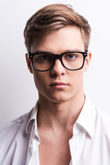 His view is knocking down. Portrait of handsome young man in eyewear looking at camera while standing against grey background