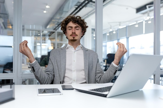 Hispanic businessman in bright white office relaxing at workplace man meditating in lotus position