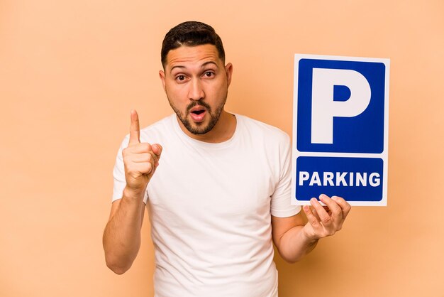 Hispanic caucasian man holding parking placard isolated on beige background having an idea inspiration concept