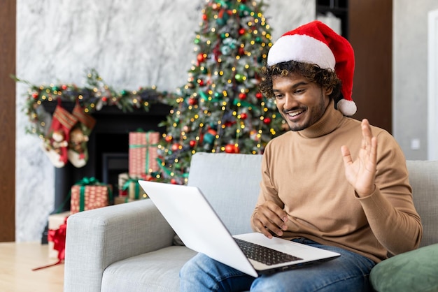 Hispanic christmas man using laptop for online video call waving at camera greeting family and