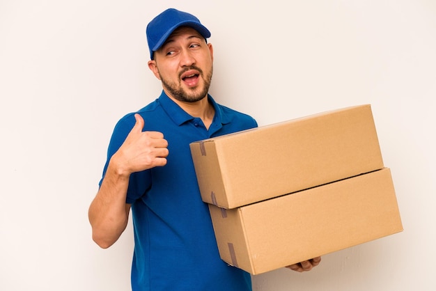 Hispanic delivery man isolated on white background points with thumb finger away laughing and carefree