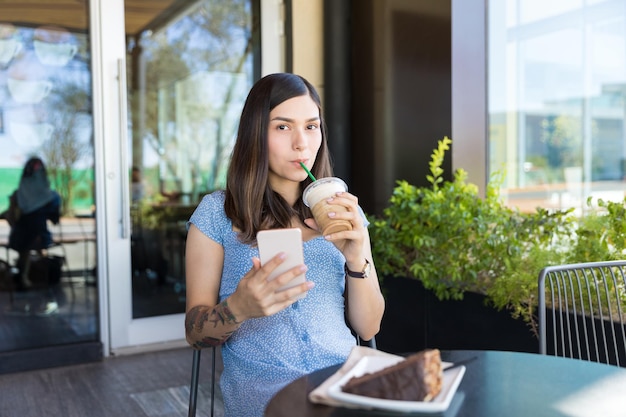 Hispanic food blogger drinking coffee while using smartphone at shopping mall