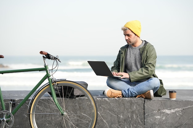 Photo hispanic freelancer working on his laptop outdoors beside a bicycle