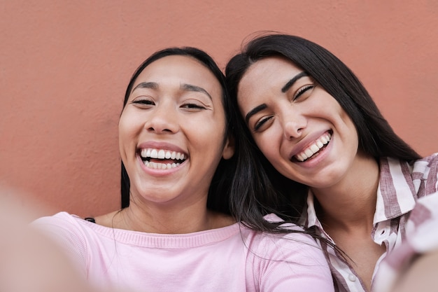 Hispanic friends having fun taking a selfie with mobile phone outdoors in the city - Focus on faces