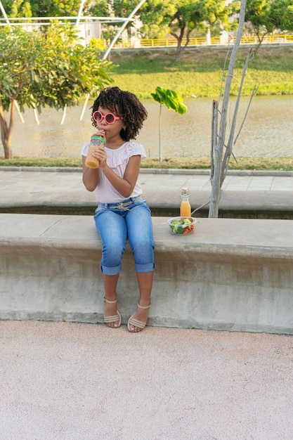 Hispanic girl in a park with a glass of healthy juice