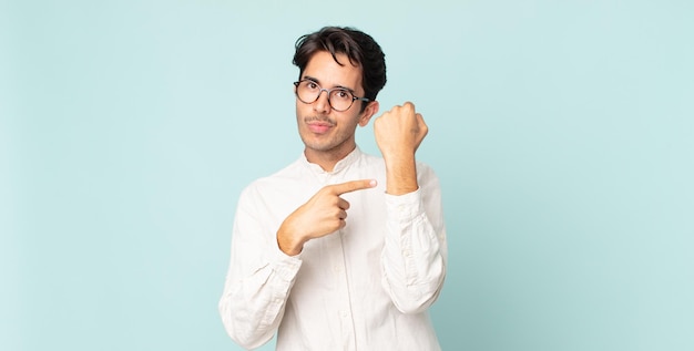 Hispanic handsome man looking impatient and angry pointing at watch asking for punctuality wants to be on time