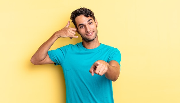 Hispanic handsome man smiling cheerfully making a call you gesture