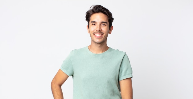 Hispanic handsome man smiling happily with a hand on hip and confident, positive, proud and friendly attitude