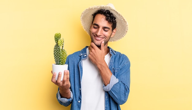 Hispanic handsome man smiling with a happy, confident expression with hand on chin farmer and cactus concept