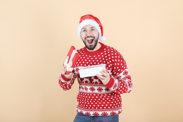 Hispanic Latino man, with Christmas hat opening a gift, beige background