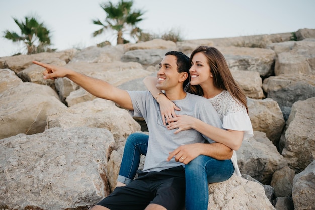 A Hispanic man is sitting with his girlfriend on the stones of a breakwater