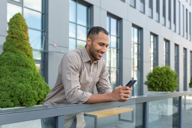 Hispanic man outside modern office building using smartphone businessman in shirt typing message and