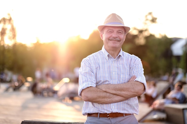 Hispanic man in summer hat with folded hands smiling looking at camera standing on city park