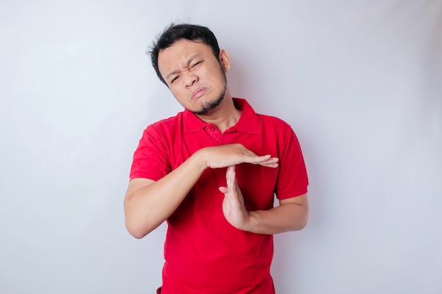 Hispanic man wearing red shirt doing time out gesture with hands frustrated and serious face