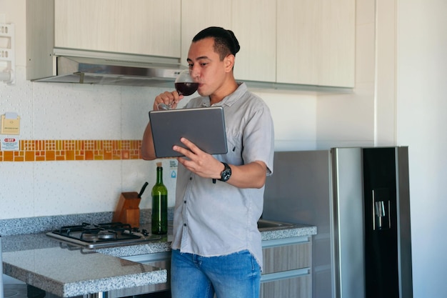 Hispanic Man with a glass of wine having a video call with a tablet at home