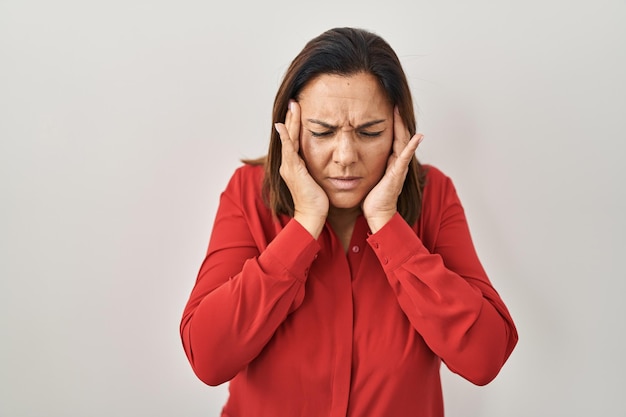 Hispanic mature woman standing over white background with hand on head for pain in head because stress. suffering migraine.