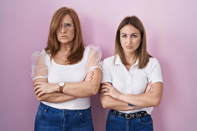 Hispanic mother and daughter wearing casual white t shirt over pink background skeptic and nervous, disapproving expression on face with crossed arms. negative person.