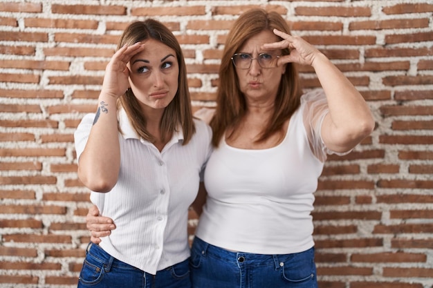 Hispanic mother and daughter wearing casual white t shirt worried and stressed about a problem with hand on forehead nervous and anxious for crisis