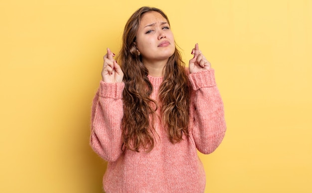 Hispanic pretty woman crossing fingers anxiously and hoping for good luck with a worried look