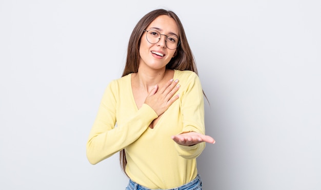 Hispanic pretty woman feeling happy and in love, smiling with one hand next to heart and the other stretched up front