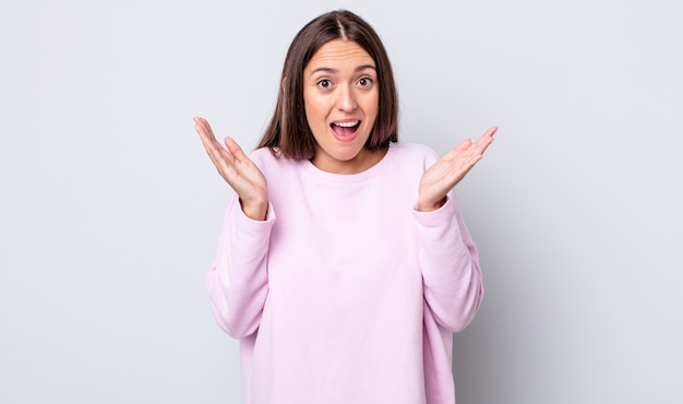 Hispanic pretty woman looking happy and excited, shocked with an unexpected surprise with both hands open next to face