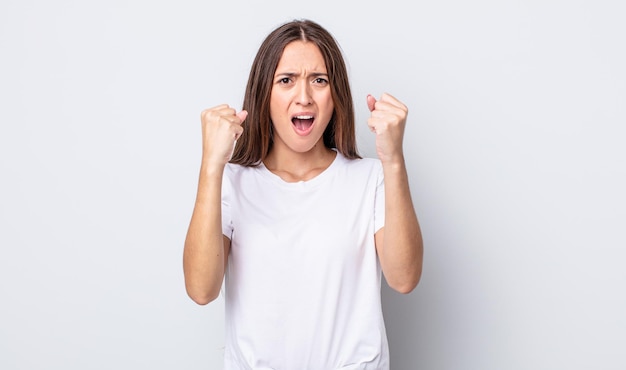 Hispanic pretty woman shouting aggressively with an angry expression or with fists clenched celebrating success