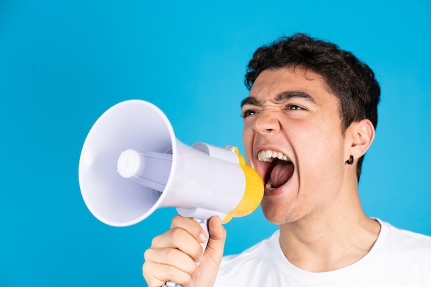 Hispanic teenager boy shouting on speaker or megaphone isolated on blue background