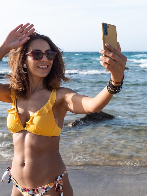 Hispanic woman on the beach making video call saying hello to the camera