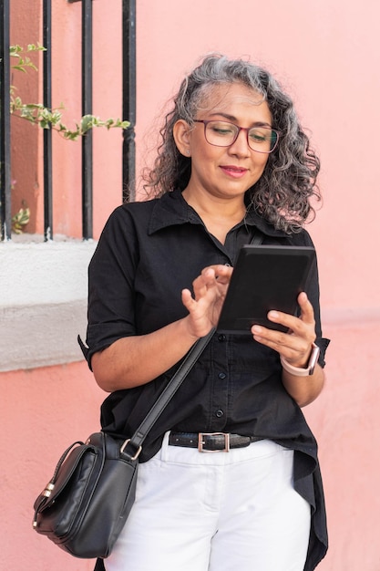 Hispanic woman in glasses holds tablet outdoors