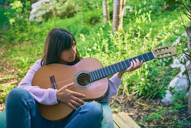 Hispanic woman holding guitar and learning to play while sitting on vintage chair on her porch