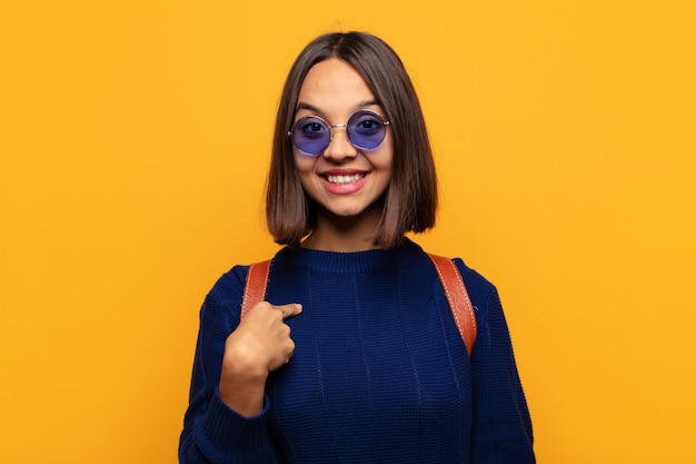 Hispanic woman looking happy, proud and surprised, cheerfully pointing to self, feeling confident and lofty