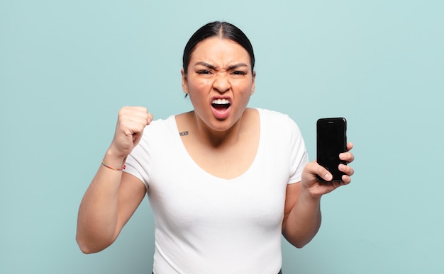 Hispanic woman shouting aggressively with an angry expression or with fists clenched celebrating success