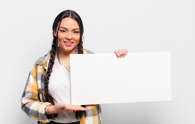 Hispanic woman smiling cheerfully, feeling happy and showing a concept in copy space with palm of hand