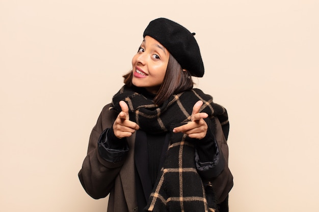 Hispanic woman smiling with a positive, successful, happy attitude pointing to the front, making gun sign with hands