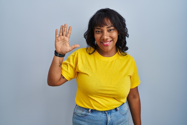 Hispanic woman standing over blue background showing and pointing up with fingers number five while smiling confident and happy.