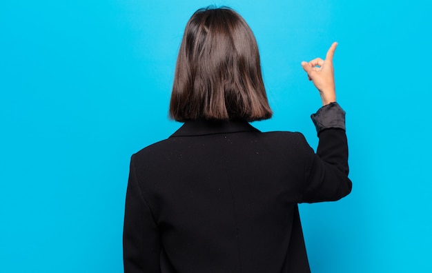 Photo hispanic woman standing and pointing to object on copy space, rear view