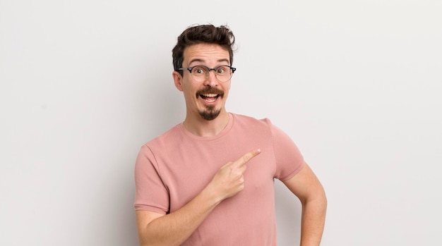 Hispanic young man looking excited and surprised pointing to the side and upwards to copy space