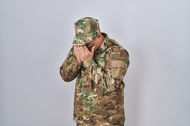 Photo hispanic young man wearing camouflage army uniform with sad expression covering face with hands while crying depression concept