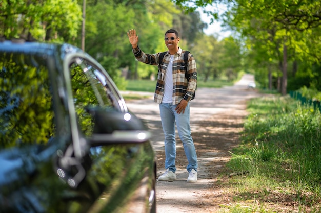 Hitchhiking. Young man in plaid shirt hitchhiking in the countryside