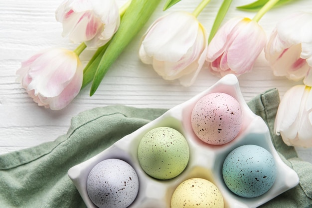 Holder with Easter eggs painted pastel colors on a white wooden background