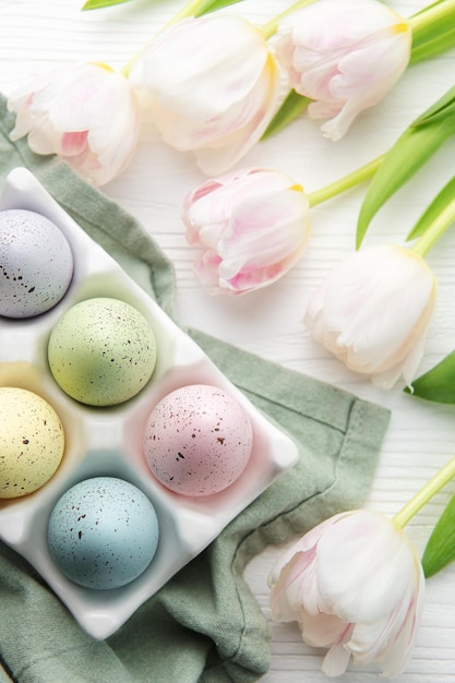 Holder with Easter eggs painted pastel colors on a white wooden background