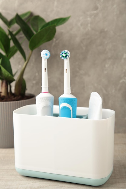 Holder with modern electric toothbrushes and plant on blue background