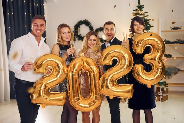 Holding balloons with 2023 number Group of people have a new year party indoors together