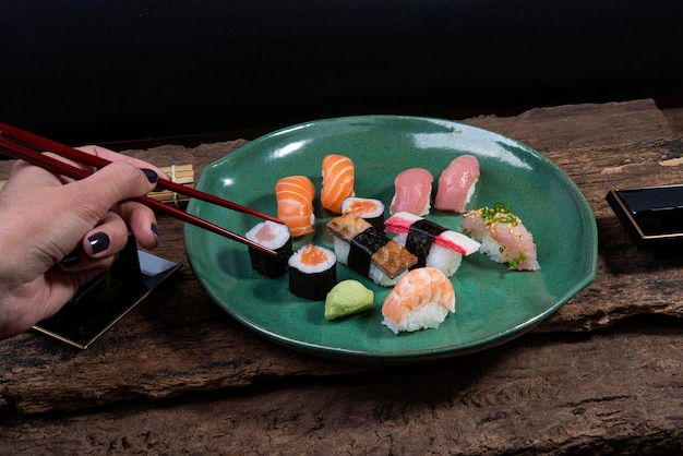 Holding chopsticks nigiri sushi and hossomaki salmon tuna kanikama skin shrimp sake soy sauce