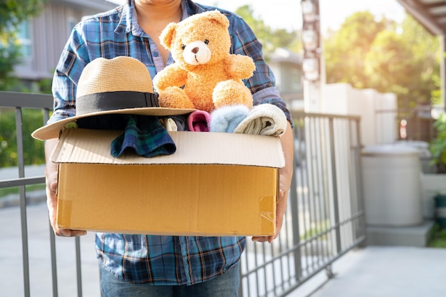 Holding clothing donation box with used clothes and doll at home to support help for poor people in the world