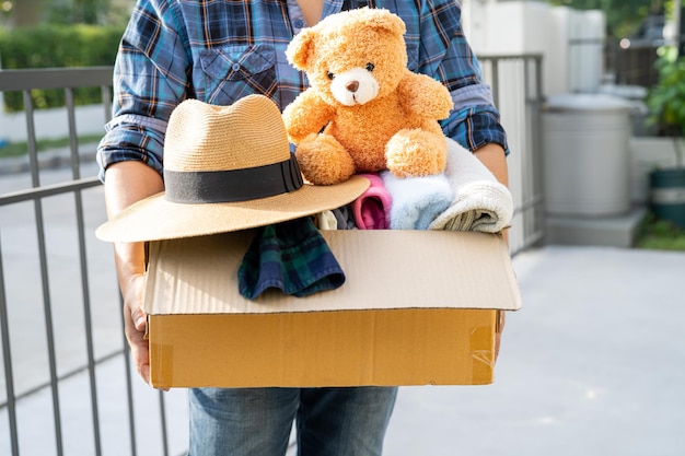 Holding clothing donation box with used clothes and doll at home to support help for poor people in the world